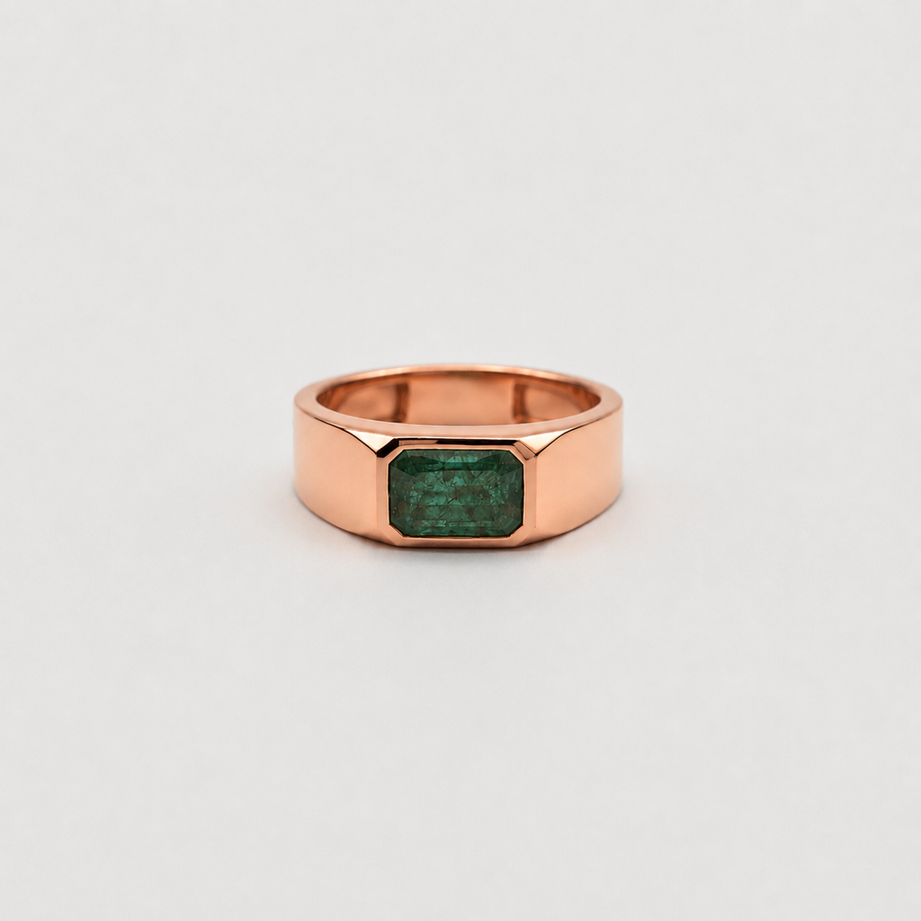 A rose gold ring with a faceted octagonal band and a rectangular green emerald-cut gemstone, shown on a light gray background.