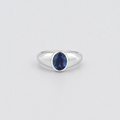 A silver ring featuring a marquise-cut deep blue gemstone in a bezel setting, centered on a light gray background.