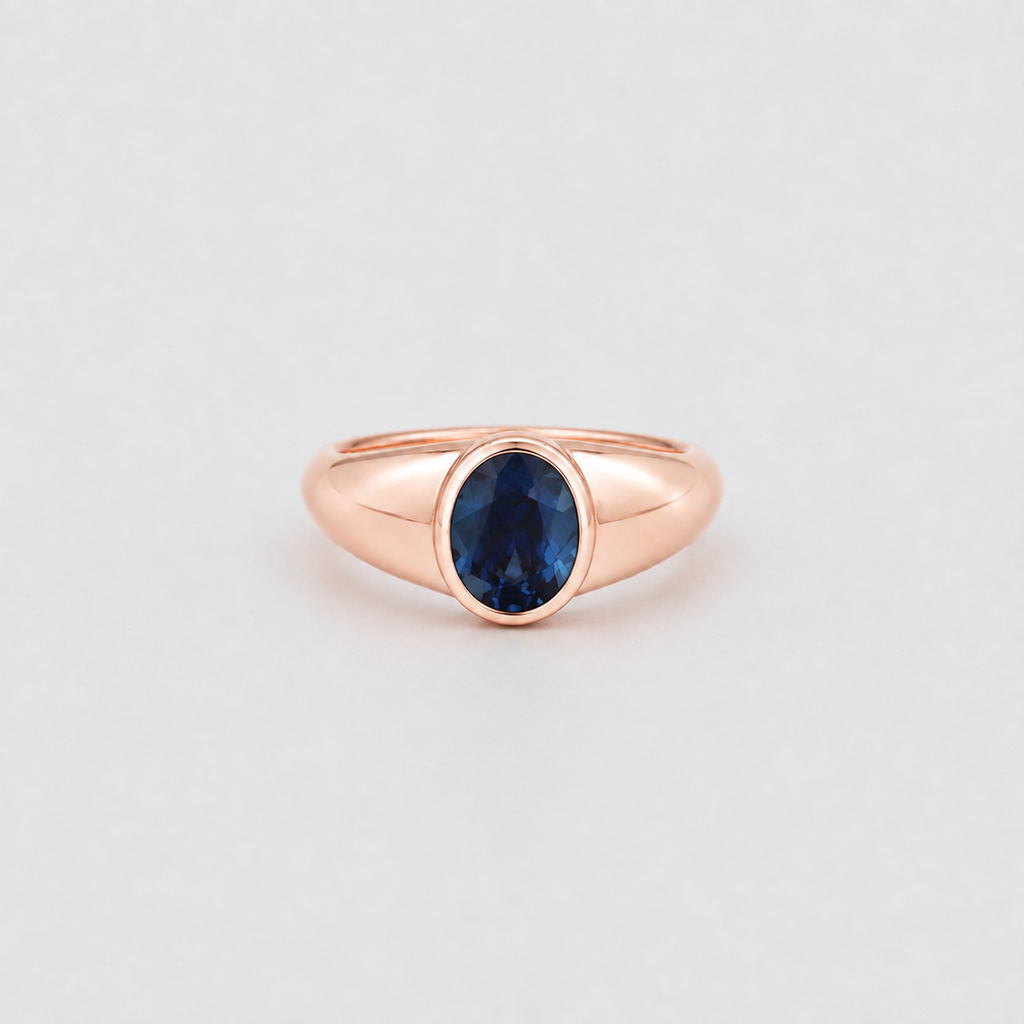 A rose gold ring featuring an oval-cut dark blue gemstone in a bezel setting, centered against a light gray background.