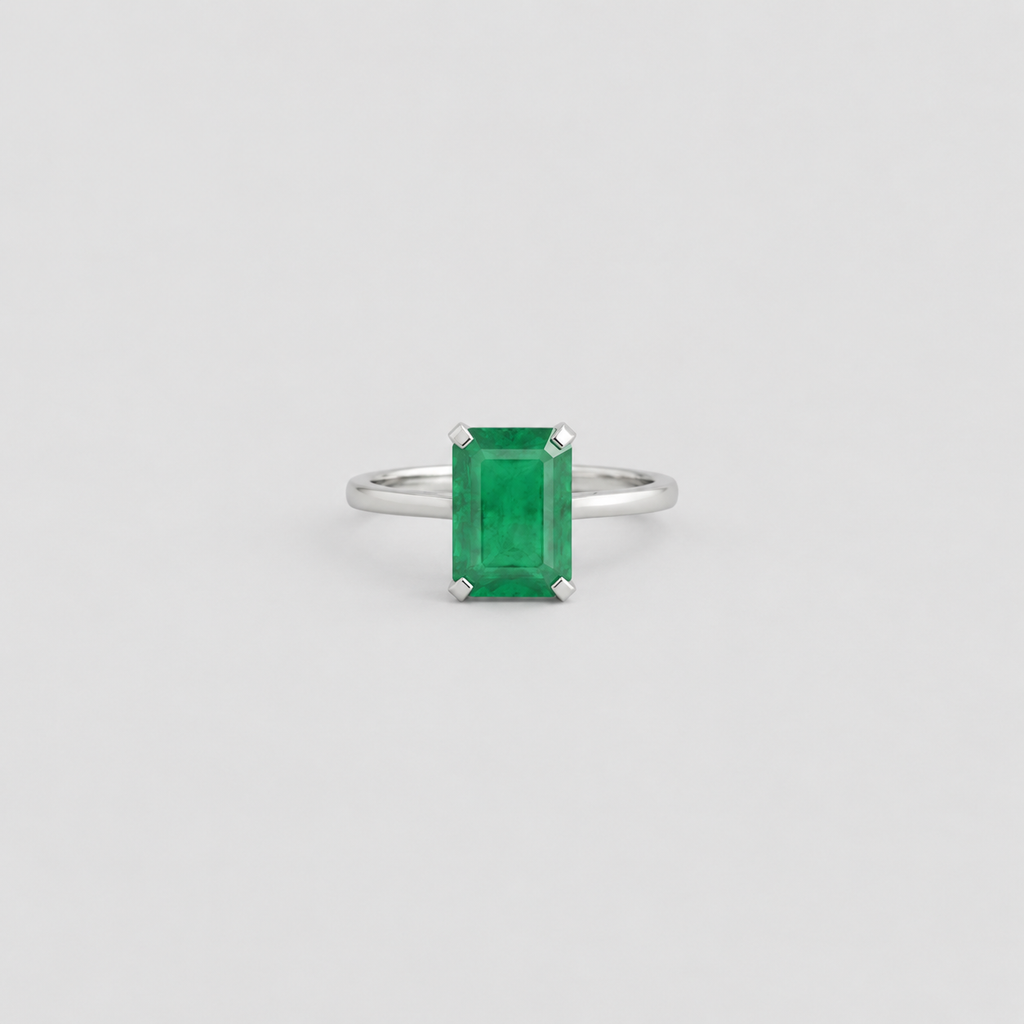 An emerald-cut green gemstone ring set in a polished silver band, centered against a light gray background.