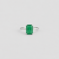 An emerald-cut green gemstone ring set in a polished silver band, centered against a light gray background.