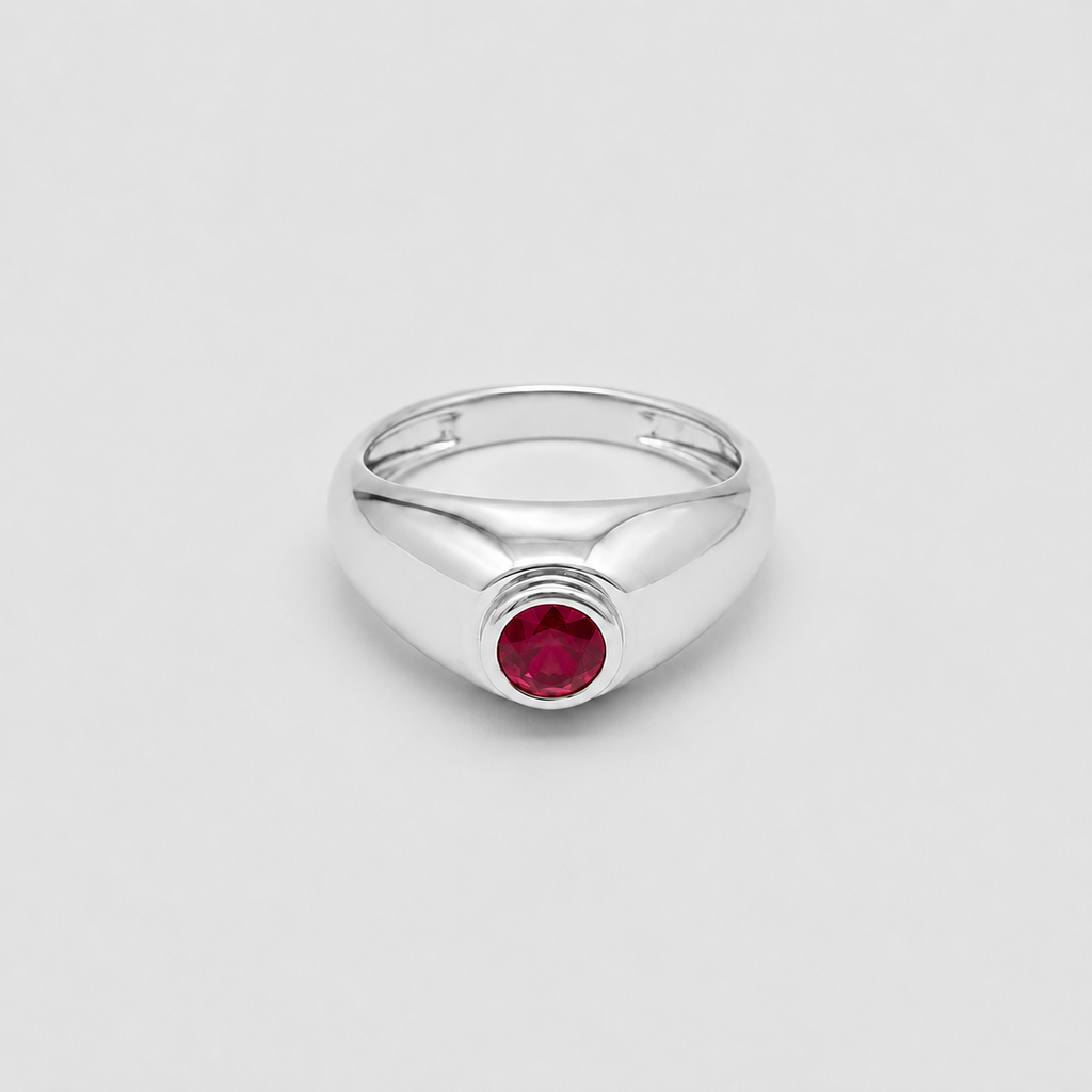 A polished silver signet-style ring with a round red gemstone in the center, photographed on a clean light gray background.
