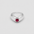 A polished silver signet-style ring with a round red gemstone in the center, photographed on a clean light gray background.