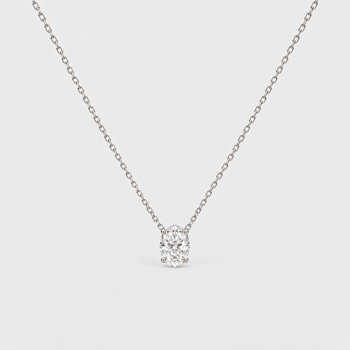 A delicate silver chain necklace with a small, clear round-cut gemstone pendant set in a prong setting, shown against a light gray background.