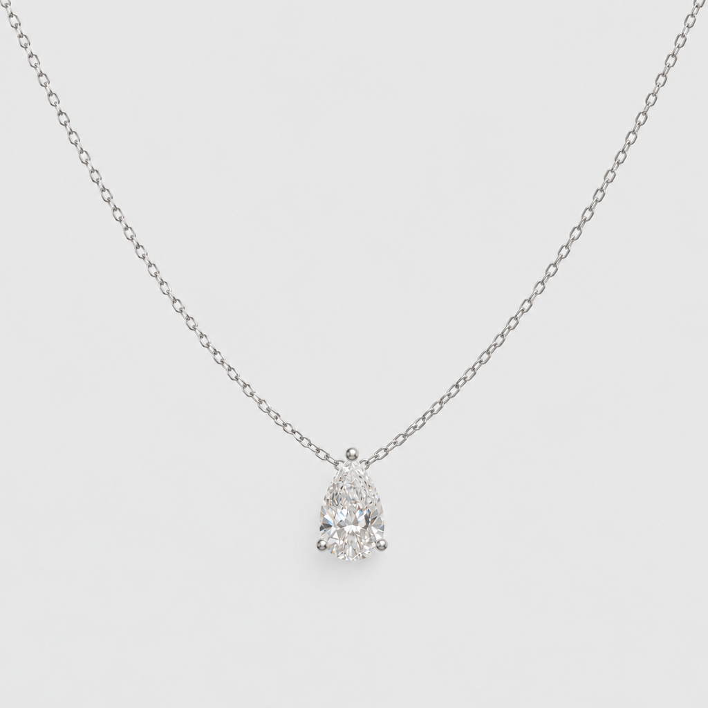 A delicate silver chain necklace with a pear-cut diamond pendant in a prong setting, displayed against a light gray background.