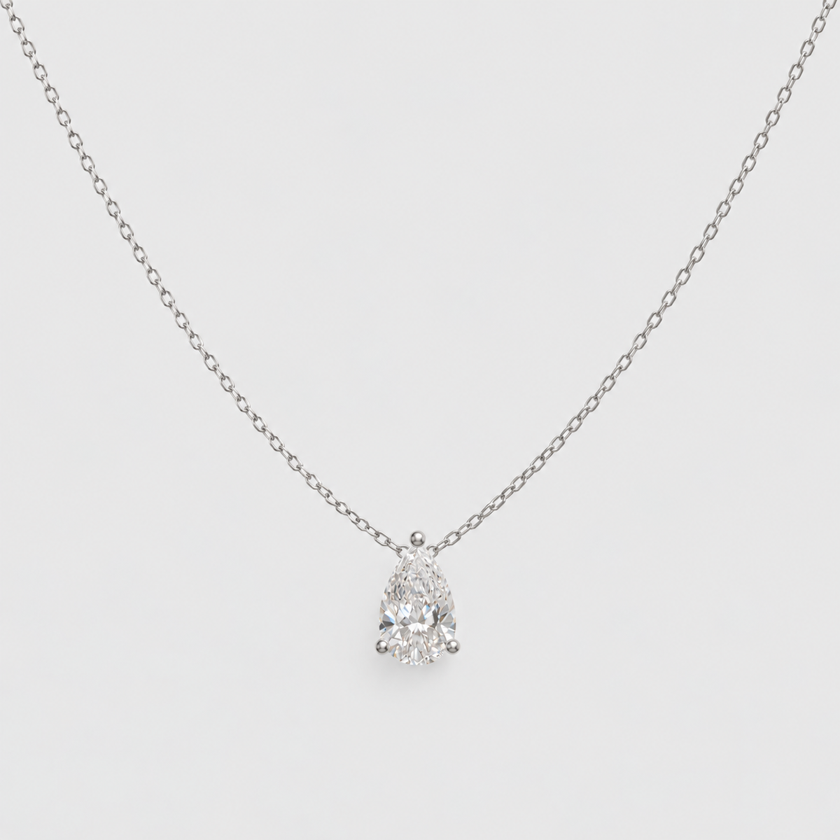 A delicate silver chain necklace with a pear-cut diamond pendant in a prong setting, displayed against a light gray background.