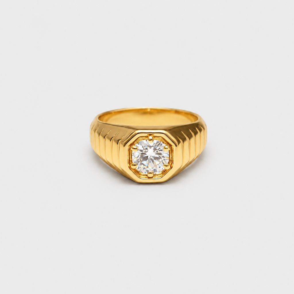 A gold signet-style ring with a faceted octagonal bezel holding a round clear gemstone, shown on a plain light gray background.