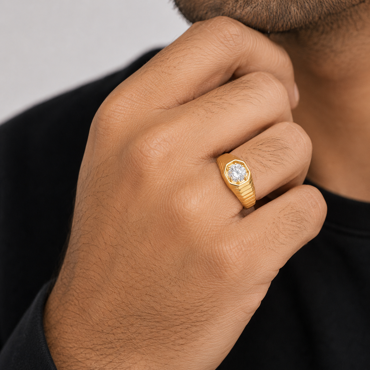 A close-up of a man's hand wearing a gold snake-bone style ring with a clear round gemstone, set against a dark shirt and neutral background.