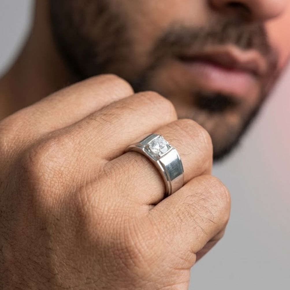 Close-up of a hand wearing a silver ring with a diamond on a neutral background