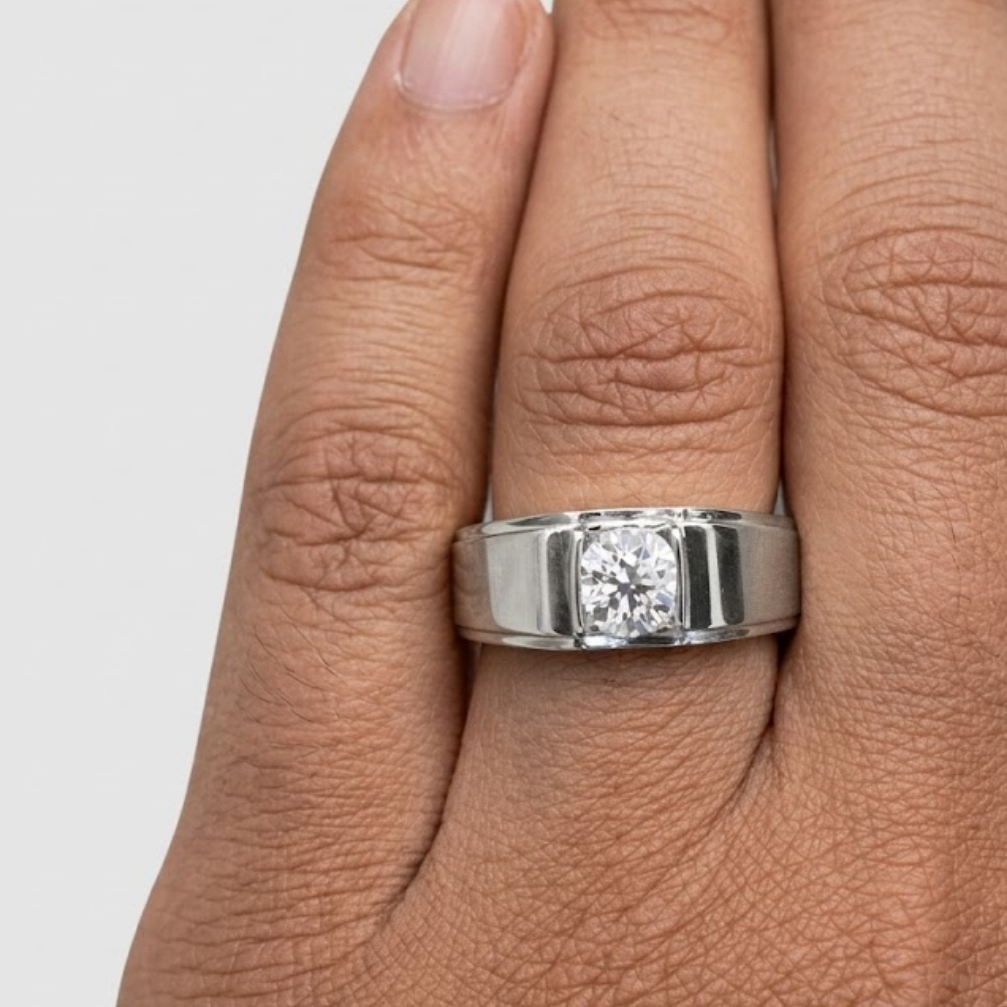 Silver ring with a diamond on a person's finger against a light gray background