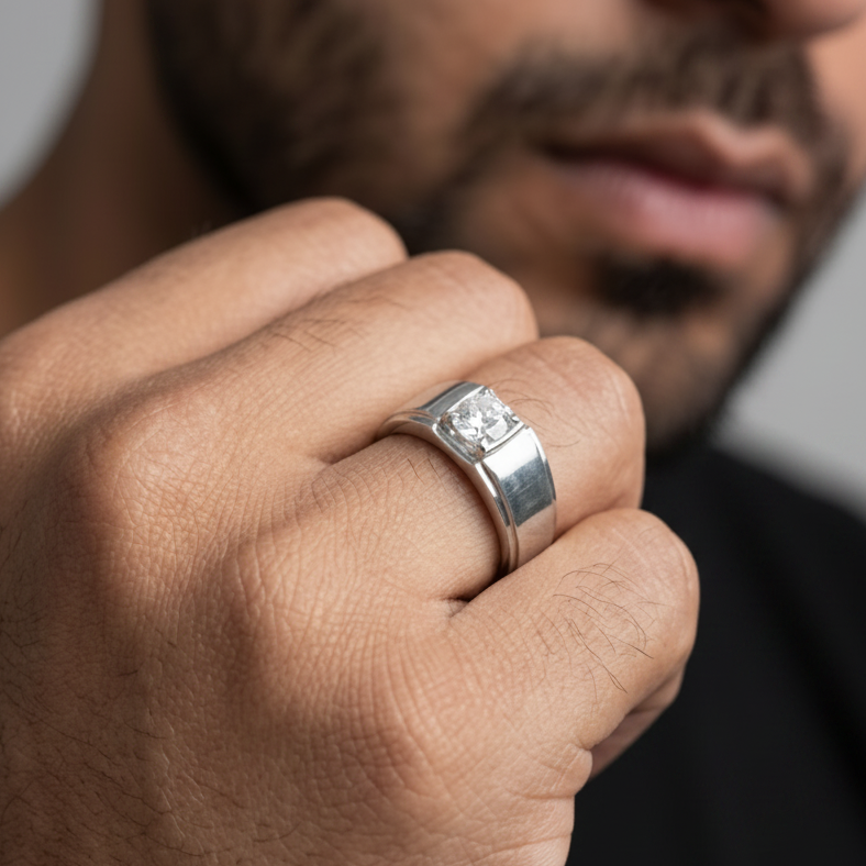 A close-up of a man's hand wearing a silver-toned men's ring with a square-cut clear gemstone, with his face blurred in the background.