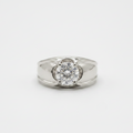 A silver ring featuring a round-cut clear gemstone in a four-prong setting, with decorative curved metalwork on either side of the stone, shown on a light gray background.