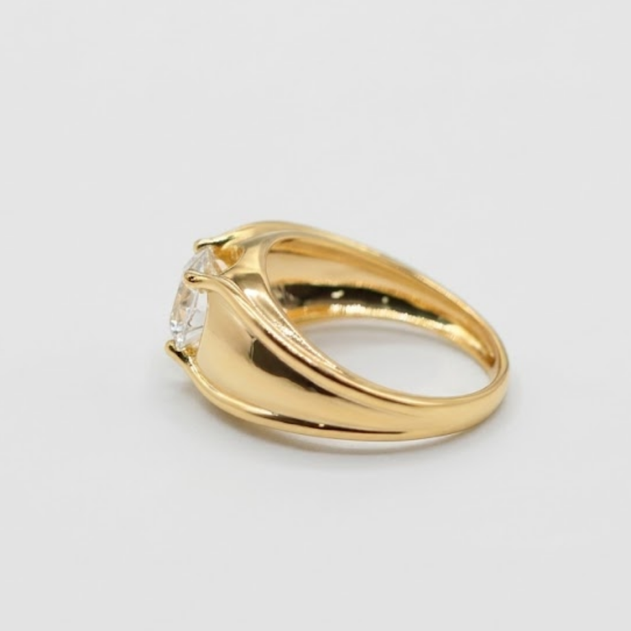 A yellow gold ring with a curved, twisted band and a small clear gemstone, shown on a plain light gray background.