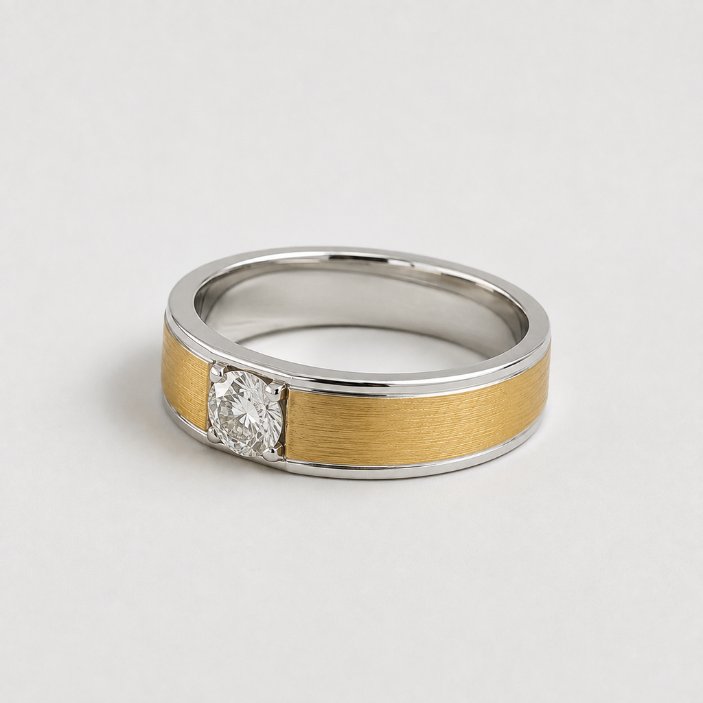 A two-tone ring band featuring a brushed gold center section, polished silver outer edges, and a single round-cut clear gemstone in a prong setting, photographed on a light gray background.