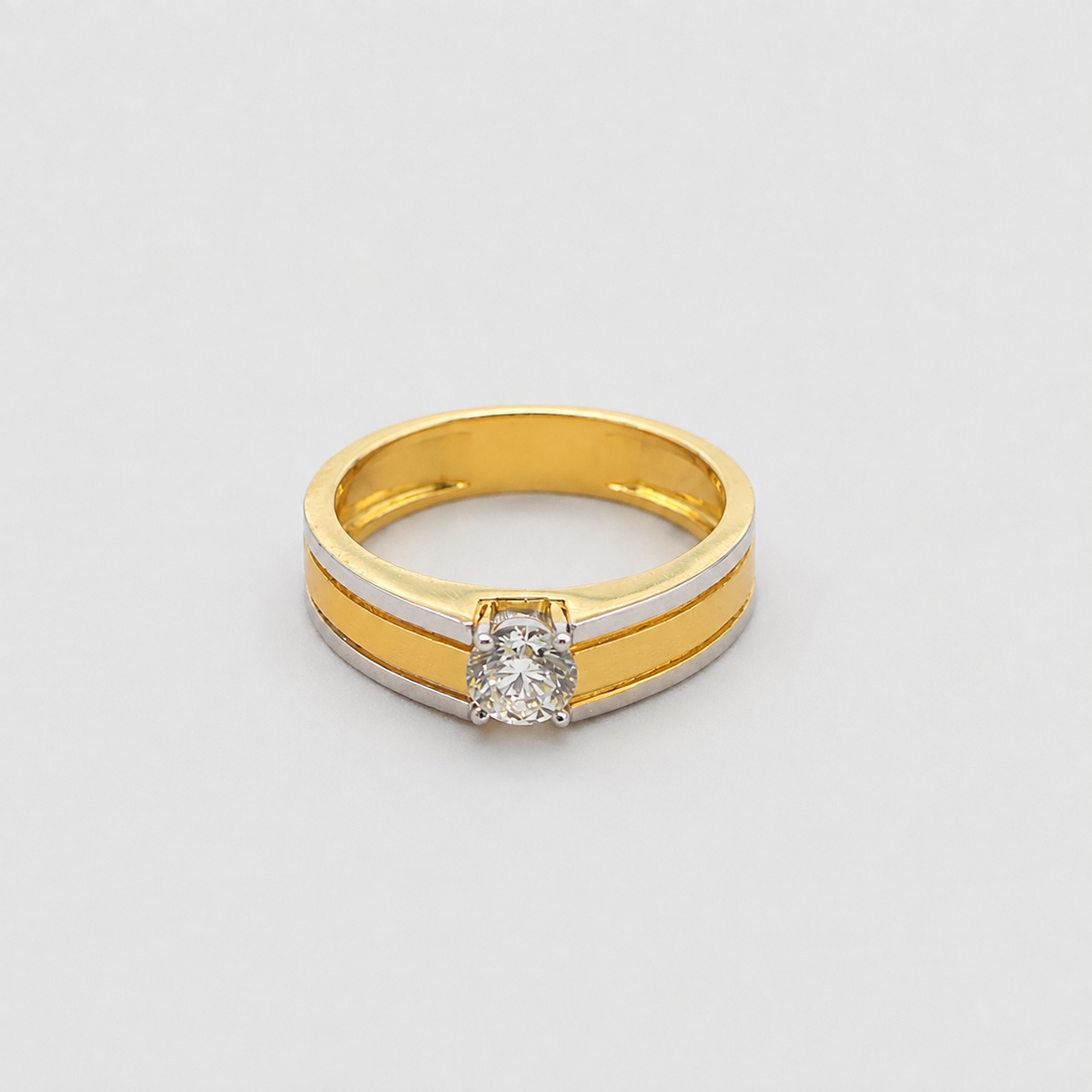A two-tone yellow gold and white gold ring featuring a round-cut clear gemstone in a prong setting, shown on a light gray background.