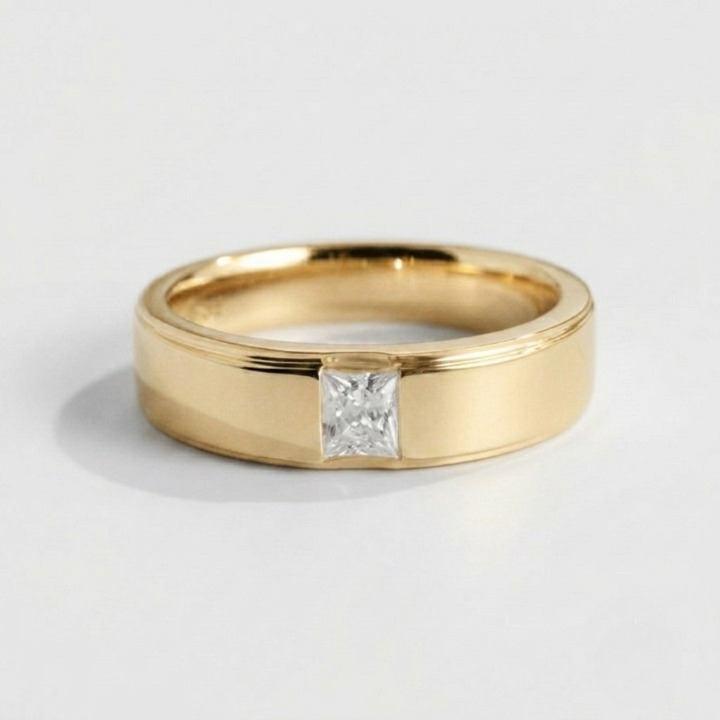 A yellow gold band ring featuring a single princess-cut diamond set in a bezel setting, photographed on a clean white background.