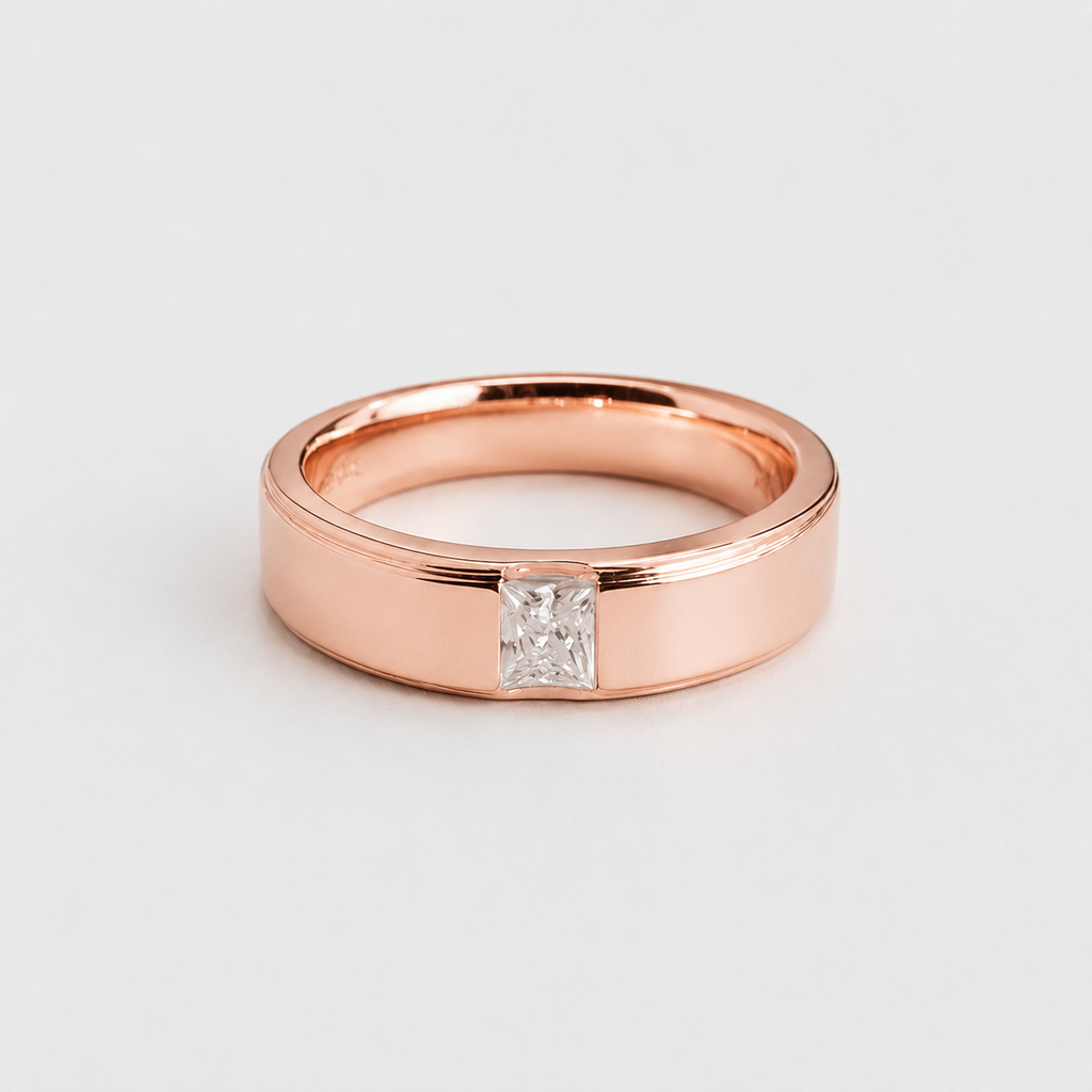 A rose gold band ring with a single princess-cut clear gemstone, photographed on a clean, light gray background.