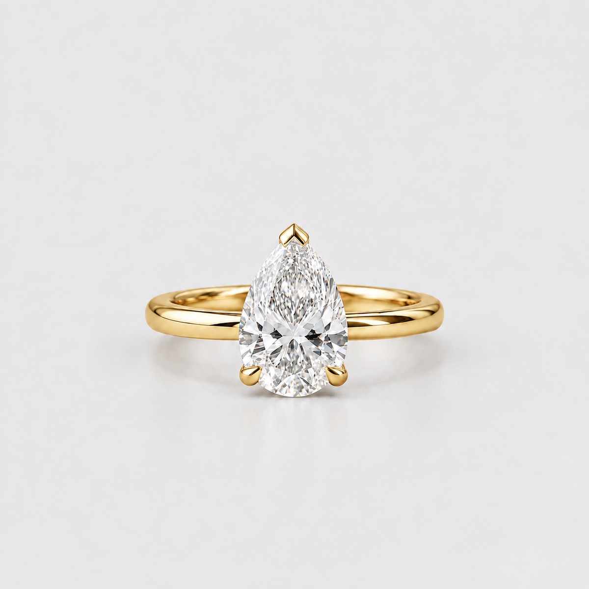 A pear-cut diamond engagement ring in a yellow gold band, photographed on a clean, light gray studio background.