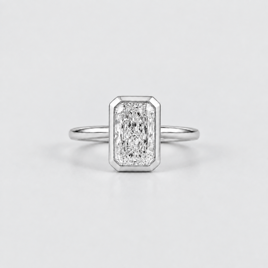 An emerald-cut diamond ring in a silver-toned metal setting with a slim band, centered on a light gray background.