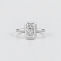 An emerald-cut diamond ring in a silver-toned metal setting with a slim band, centered on a light gray background.