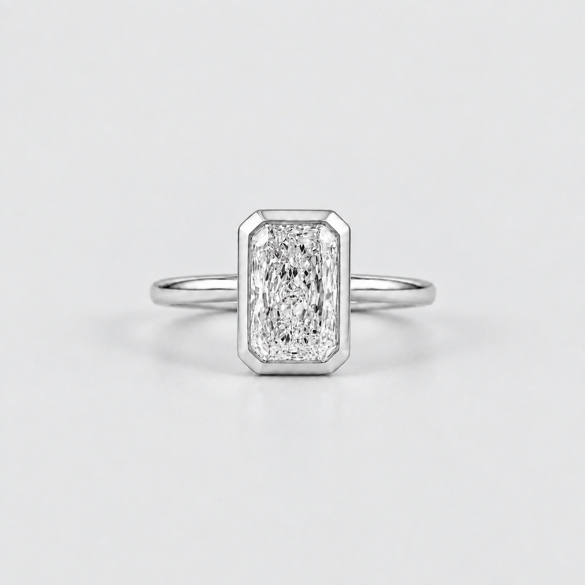 An emerald-cut diamond ring in a silver-toned metal setting with a slim band, centered on a light gray background.