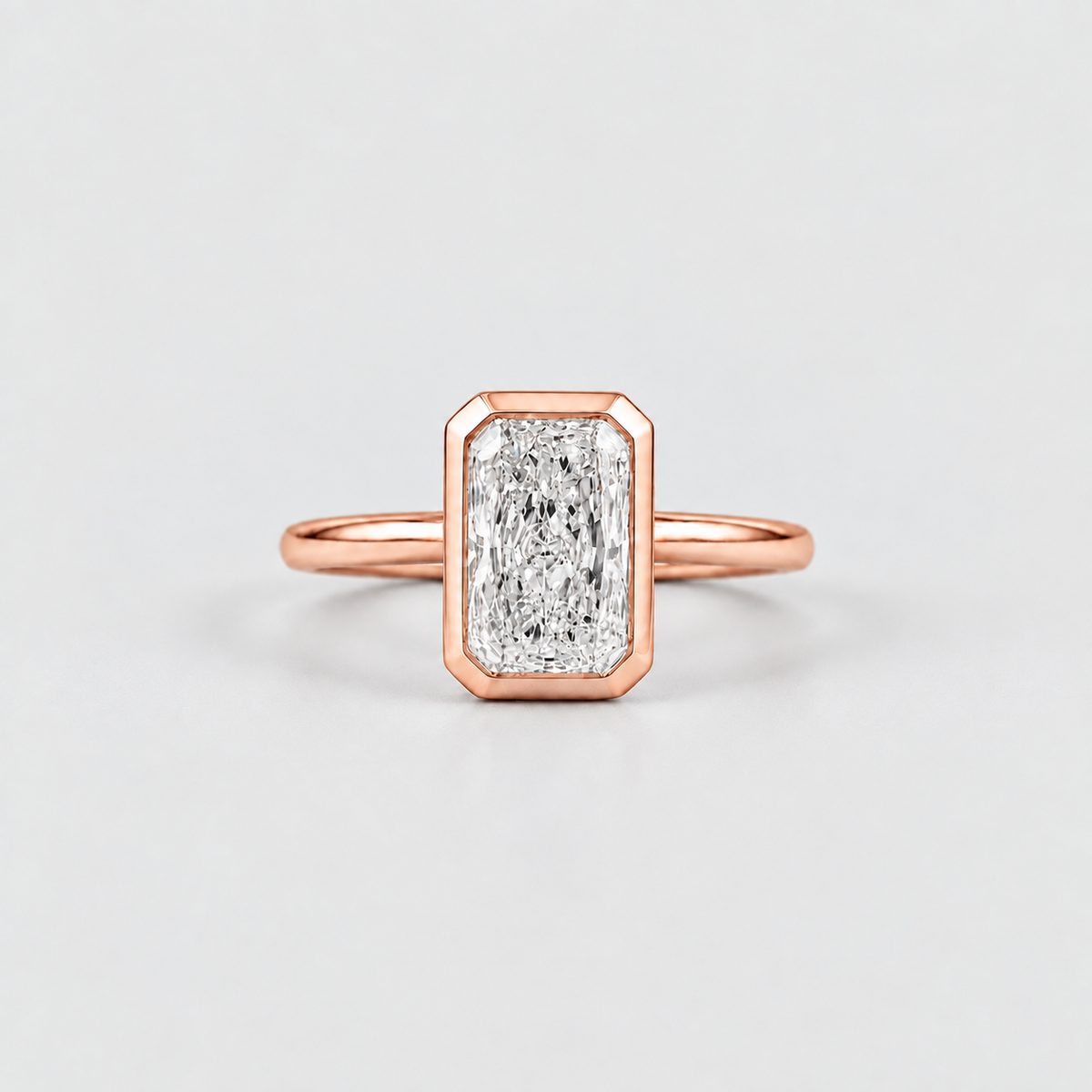 A rose gold ring featuring a rectangular baguette-cut diamond in a bezel setting, shown on a clean light gray background.