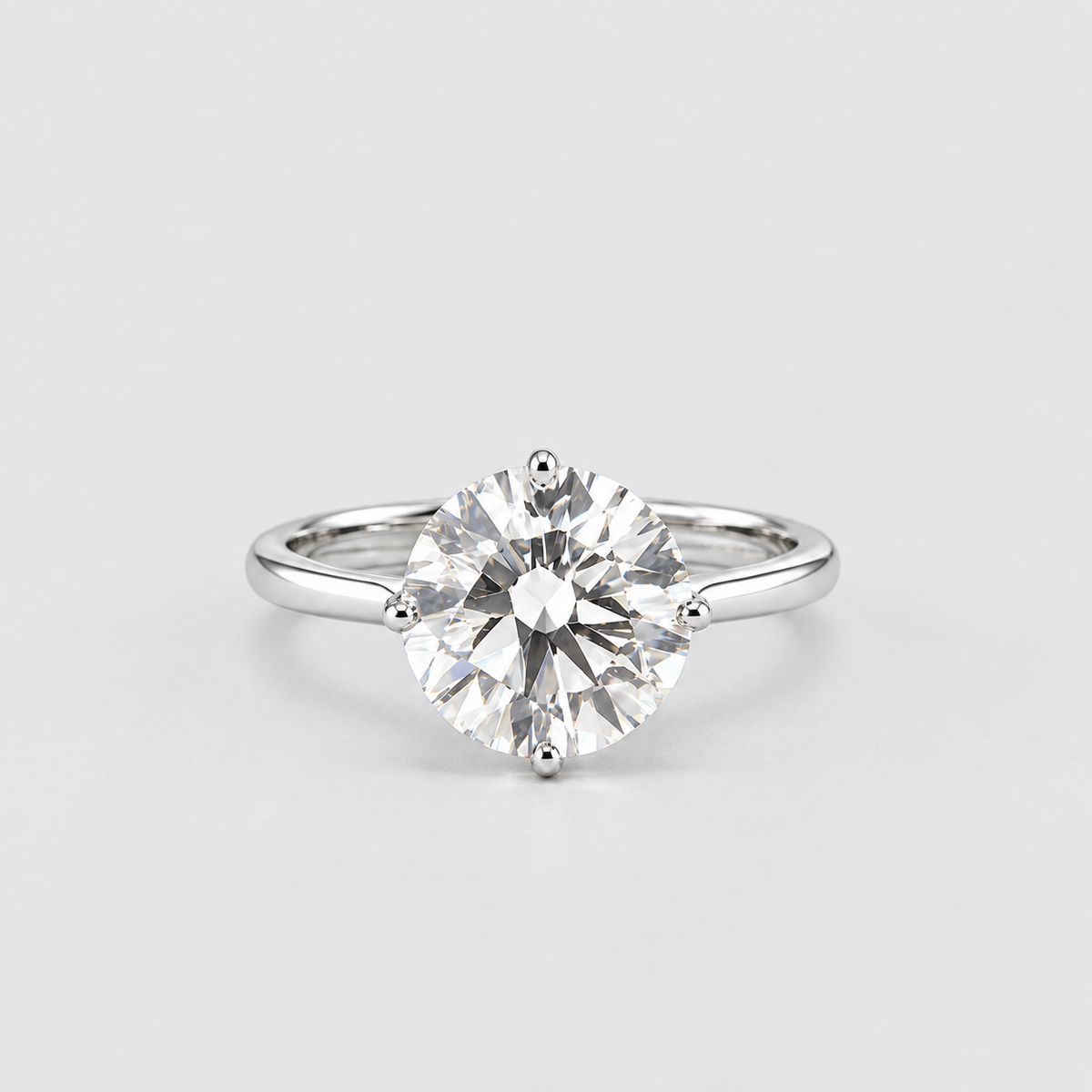 A classic solitaire engagement ring featuring a round brilliant-cut diamond set in a polished silver-colored band, photographed against a clean, light gray studio background.