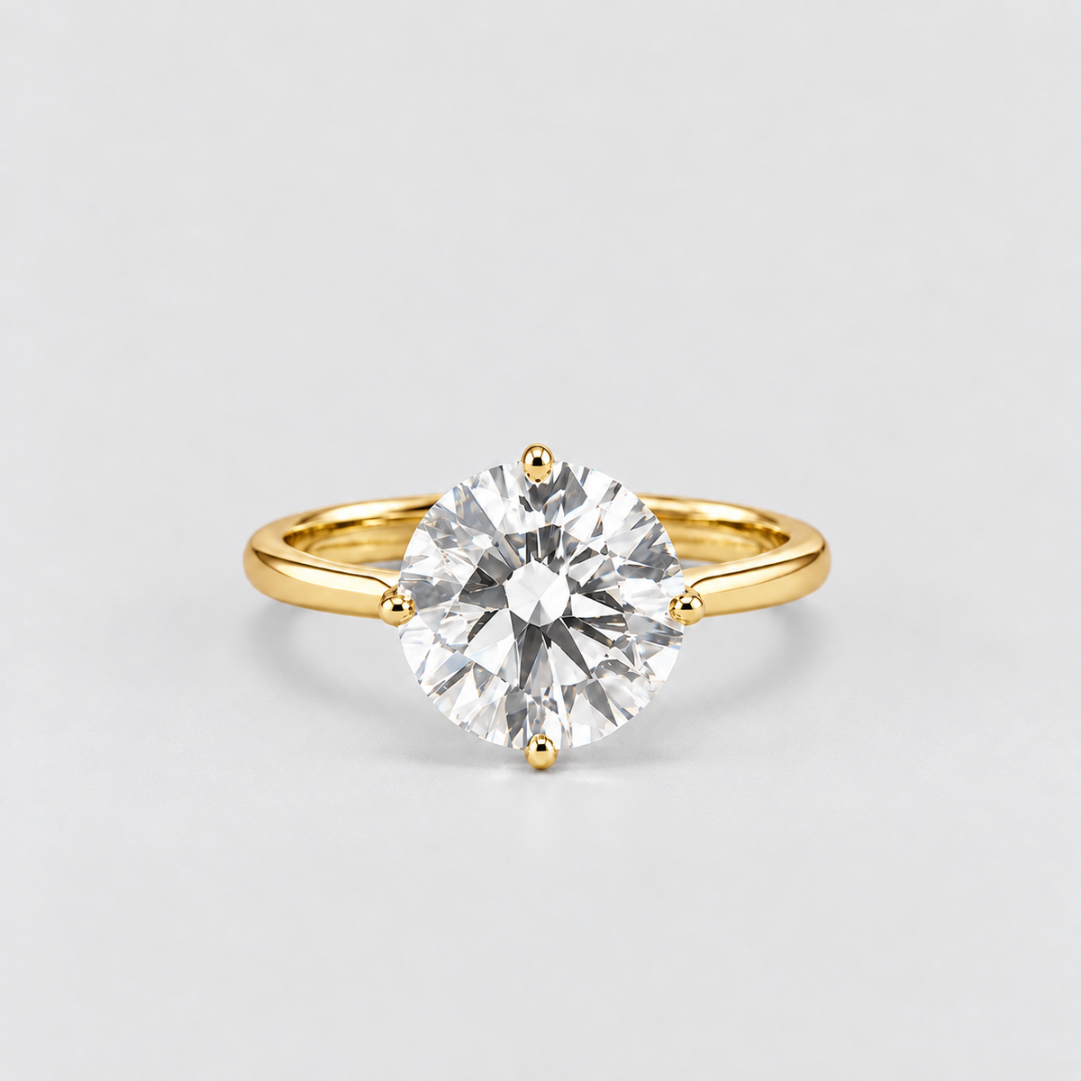 A classic solitaire engagement ring featuring a round brilliant-cut clear gemstone in a four-prong setting on a polished yellow gold band, photographed against a seamless light gray background.