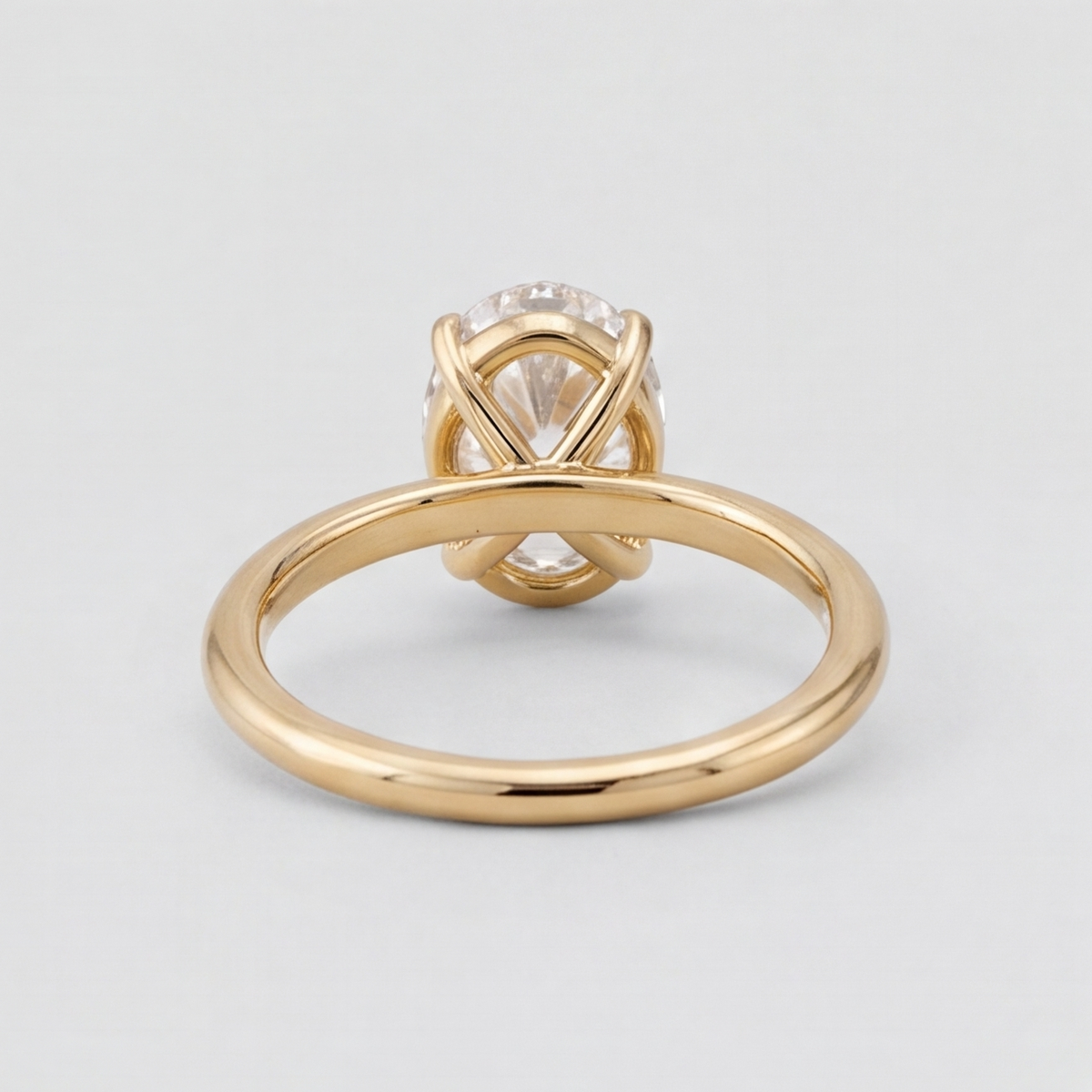 A yellow gold ring with a round clear gemstone in a crisscross setting, shown from a side angle on a light gray background.