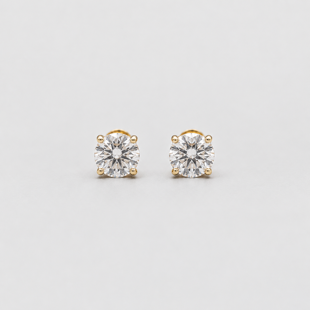 A pair of gold stud earrings with round-cut clear gemstones in a four-prong setting, photographed on a clean light gray background.