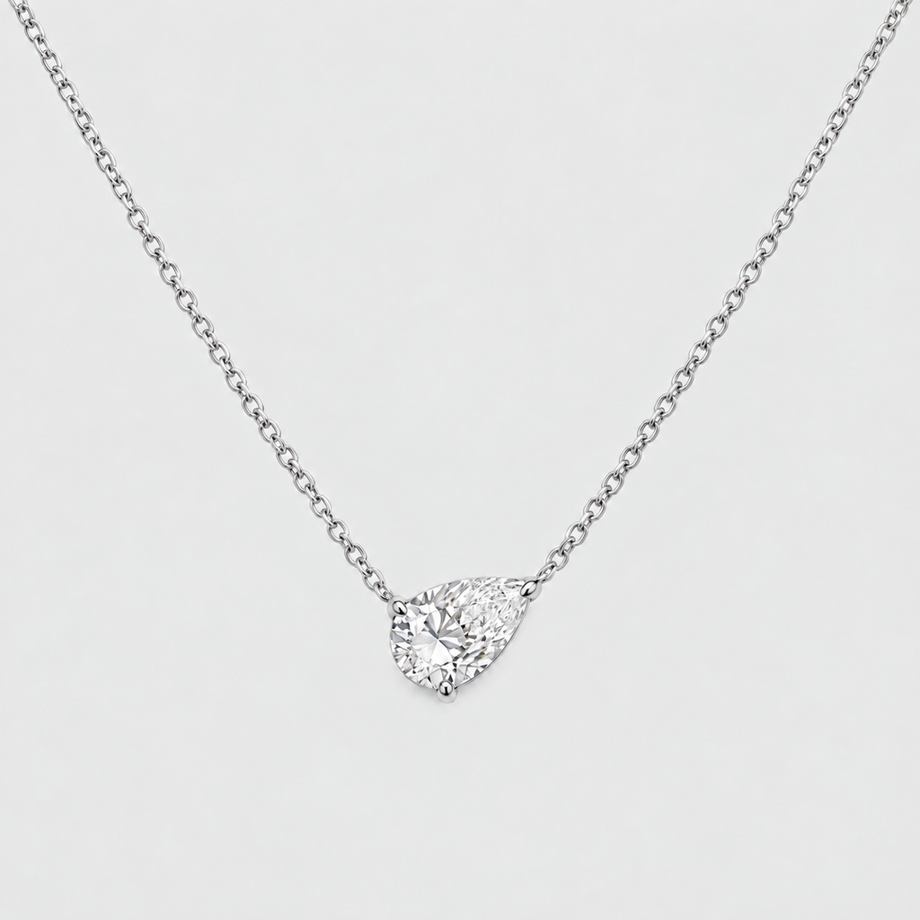 A silver-toned chain necklace with a pear-cut clear gemstone pendant in a prong setting, shown on a light gray background.