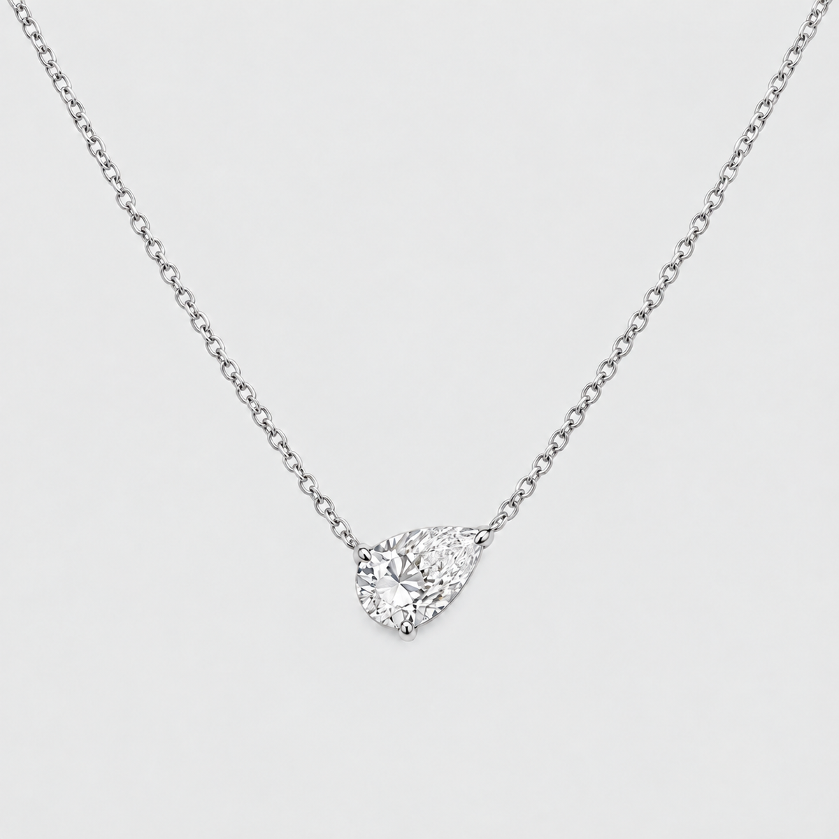 A silver-toned chain necklace with a pear-cut clear gemstone pendant in a prong setting, shown on a light gray background.