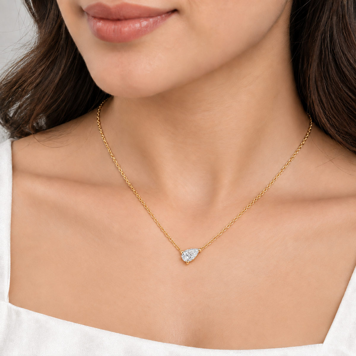 A silver-toned chain necklace with a pear-cut clear gemstone pendant. The model shows the pendant. It looks very beautiful.