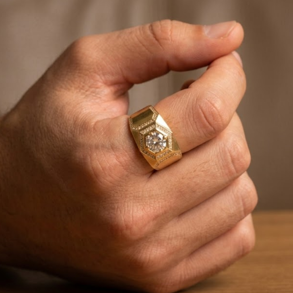 A close-up of a hand wearing a chunky yellow gold ring with a central clear gemstone, resting on a wooden surface.