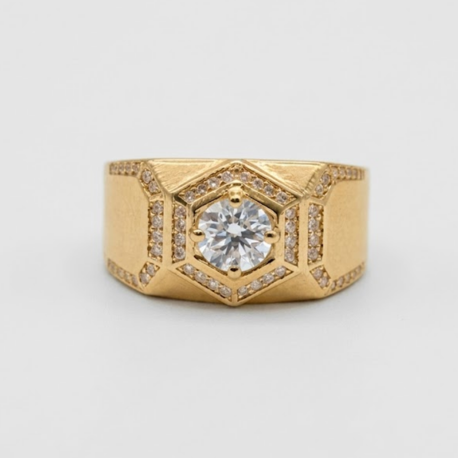 A gold geometric ring featuring a central round-cut diamond surrounded by small pavé diamonds, set on a light gray background.