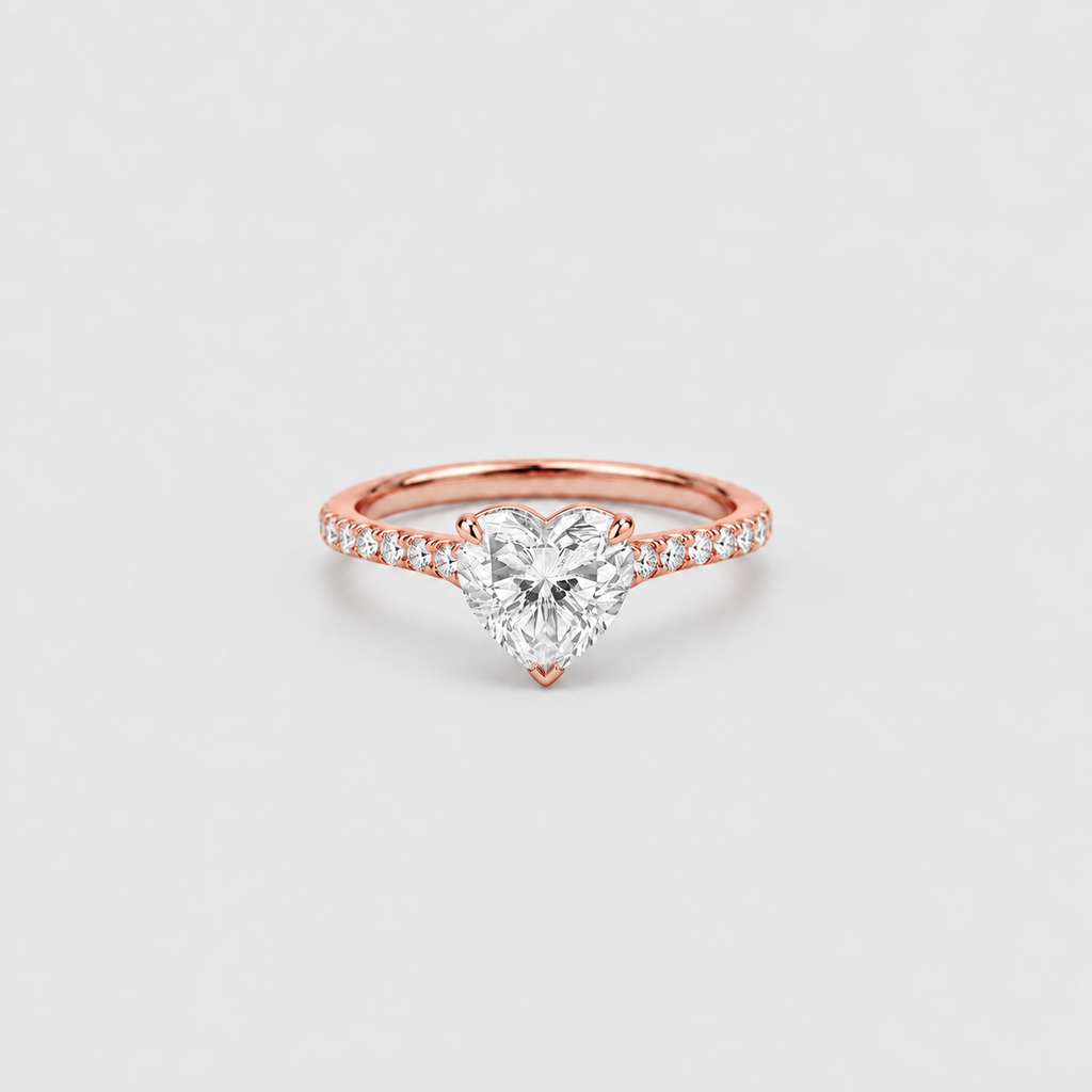 A rose gold ring featuring a heart-shaped diamond center stone and a pavé band with small round diamonds, set against a clean light gray background.