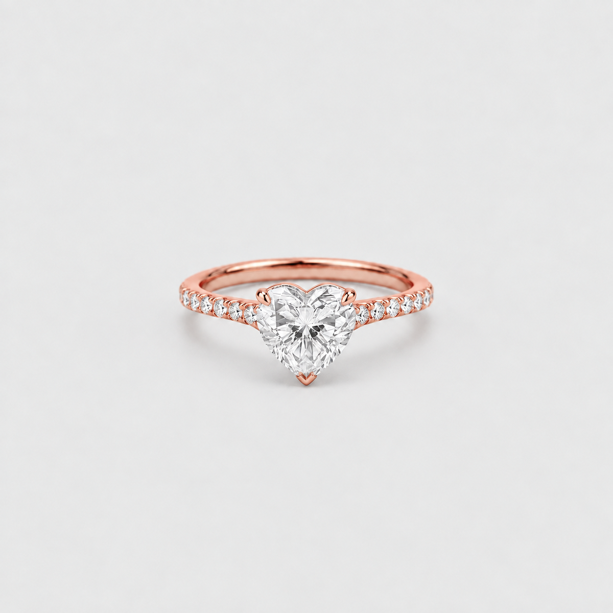 A rose gold ring featuring a heart-shaped diamond center stone and a pavé band with small round diamonds, set against a clean light gray background.