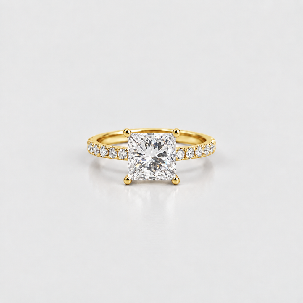 A yellow gold ring featuring a large princess-cut diamond center stone and a pavé band with small diamonds, set against a clean white background.