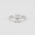 An oval-cut diamond engagement ring with a silver-toned band accented by small round diamonds, photographed on a clean light gray background.