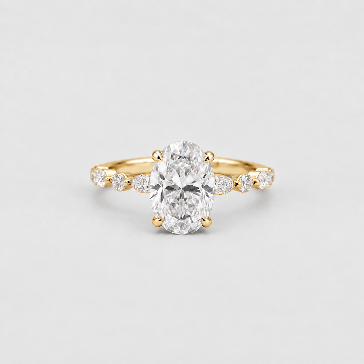 A yellow gold ring featuring a large oval-cut center diamond and smaller marquise-cut diamonds set along the shoulders, photographed on a clean light gray background.