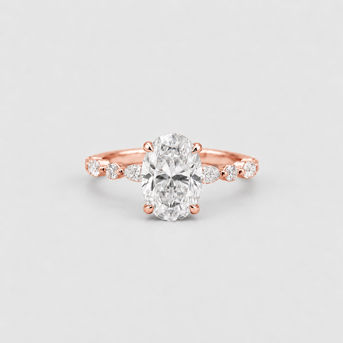 An oval-cut diamond engagement ring in a rose gold setting, featuring a diamond-accented shank, photographed on a clean light gray background.