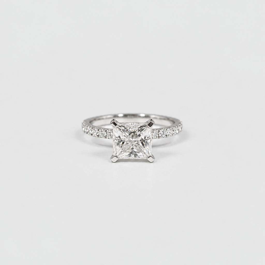 A silver engagement ring featuring a princess-cut diamond center stone and a pavé-set band, photographed on a clean white background.