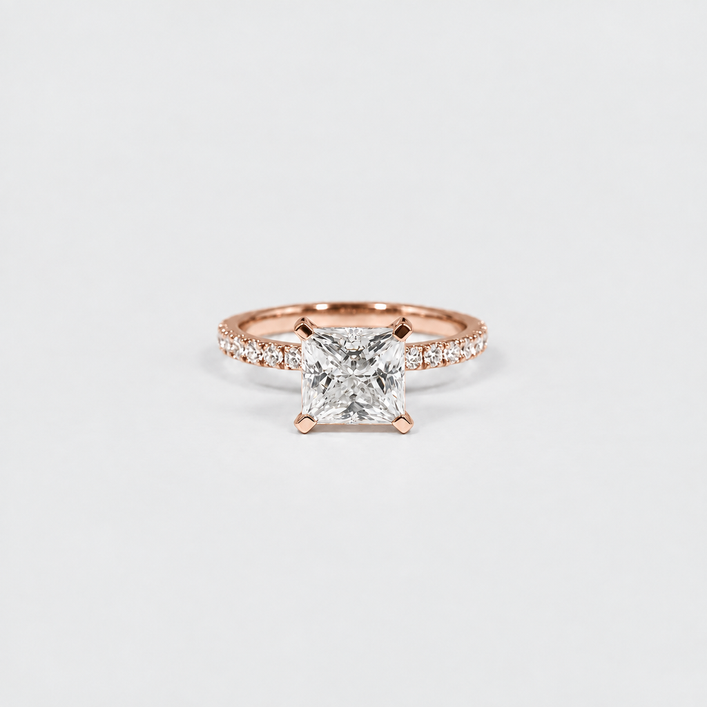 A rose gold solitaire engagement ring featuring a princess-cut diamond center stone and a pavé band, set against a clean white background.