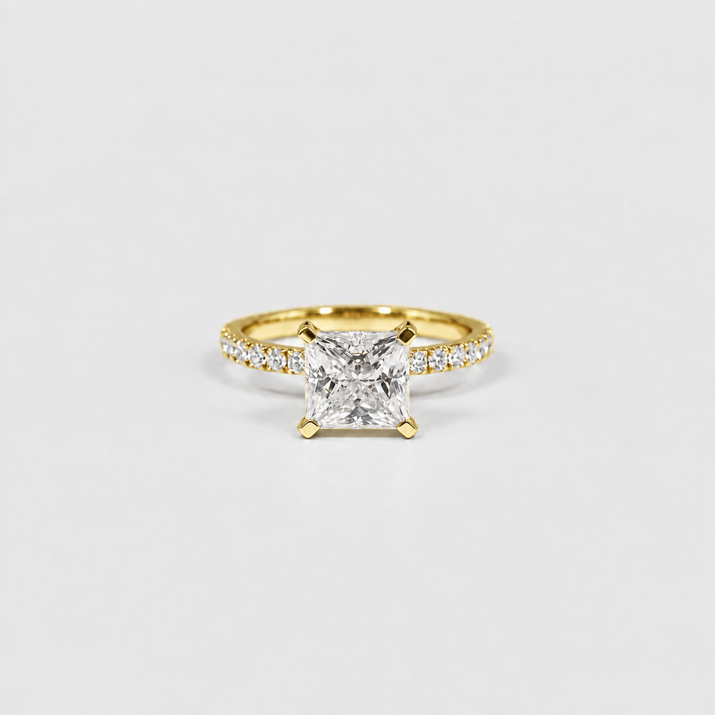 A yellow gold solitaire engagement ring featuring a princess-cut diamond center stone and a pavé diamond band, set against a clean white background.