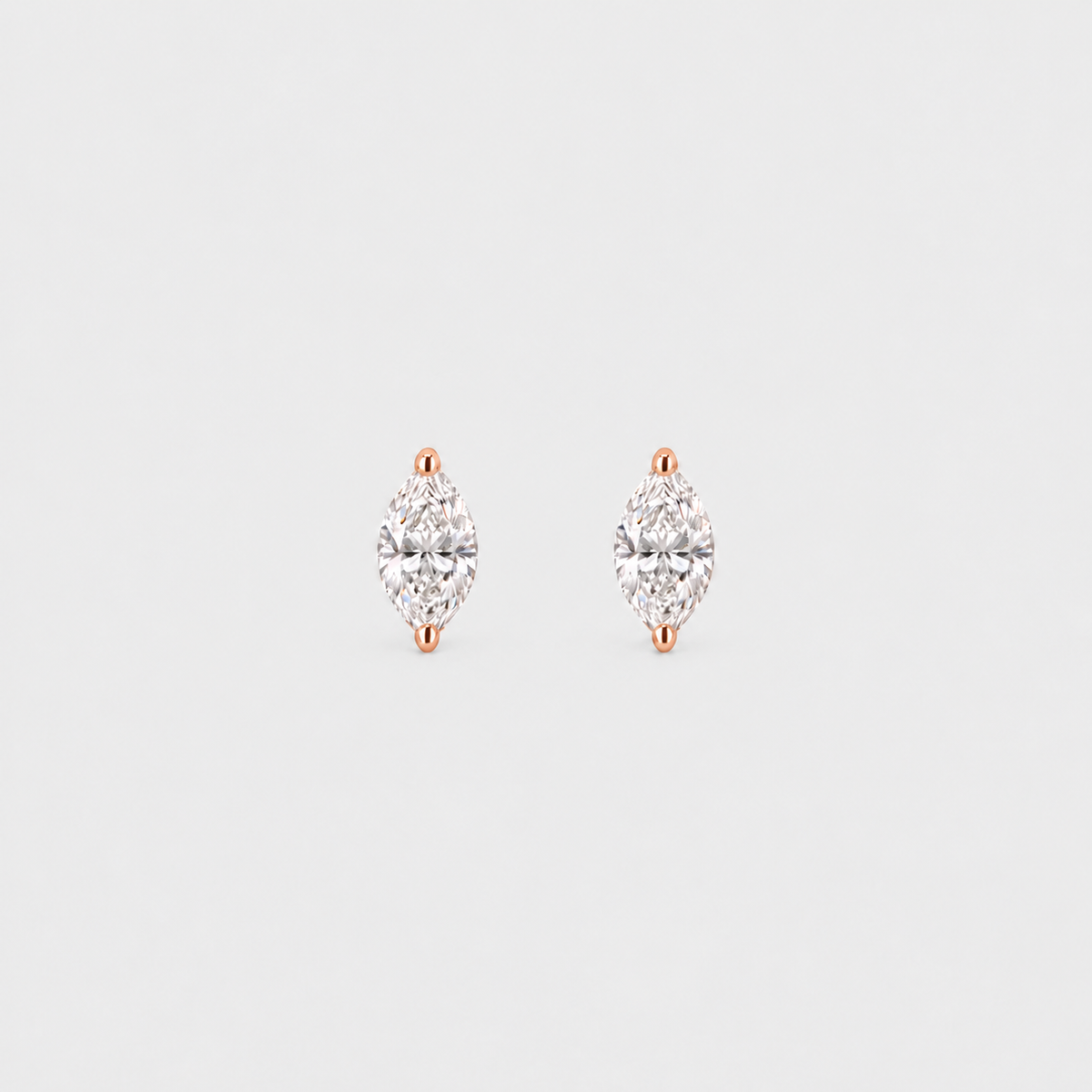 A pair of rose gold stud earrings with marquise-cut clear gemstones, set against a solid light gray background.