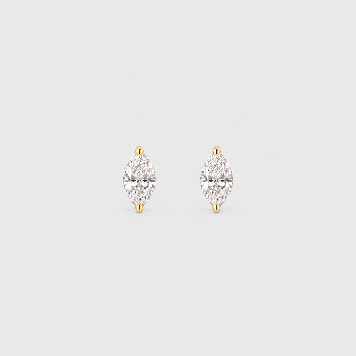 A pair of gold stud earrings with marquise-cut clear gemstones, set in a silver-toned prong setting on a light gray background.