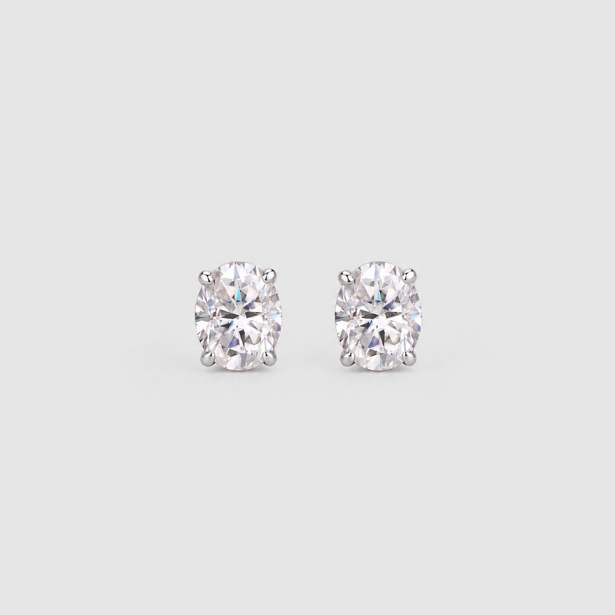 A pair of oval-cut diamond stud earrings in a four-prong setting on a light gray background.