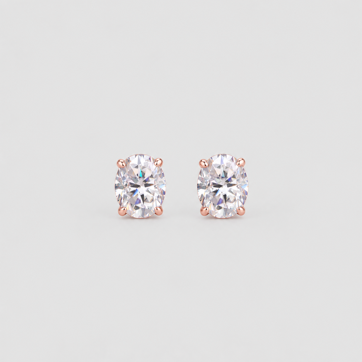 A pair of oval-cut diamond stud earrings in a rose gold four-prong setting, displayed on a clean light gray background.