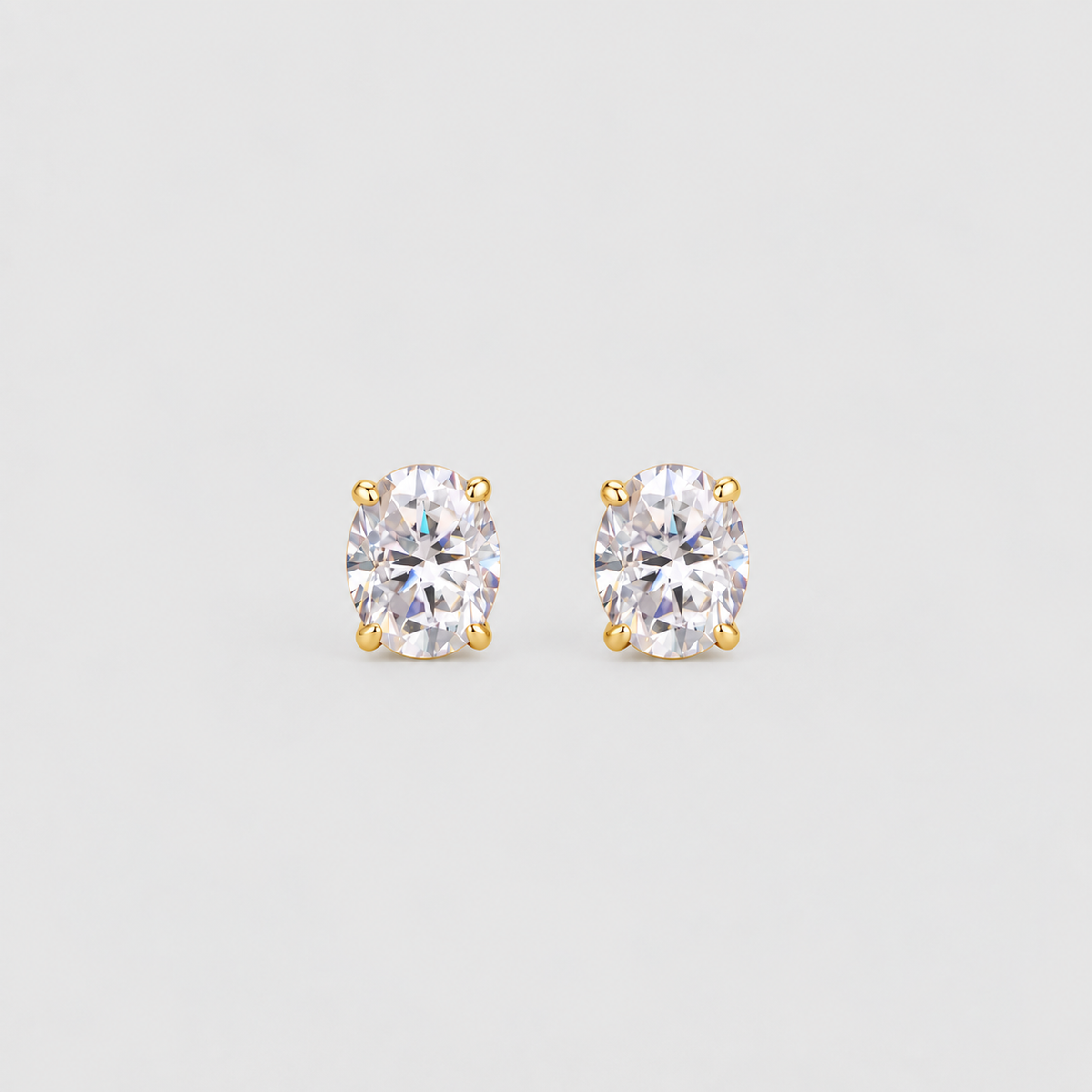A pair of oval-cut diamond stud earrings in a yellow gold four-prong setting, displayed on a clean light gray background.