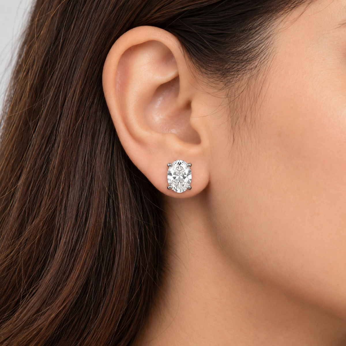 A close-up of a woman's ear wearing a single round brilliant-cut diamond stud earring in a silver setting.